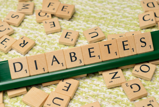 Wooden letter tiles on a green rack spelling out the word "DIABETES" against a scattered tile background.
