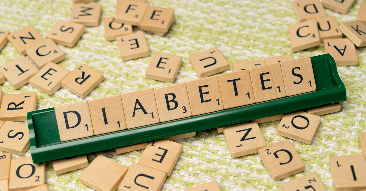 Wooden letter tiles on a green rack spelling out the word "DIABETES" against a scattered tile background.