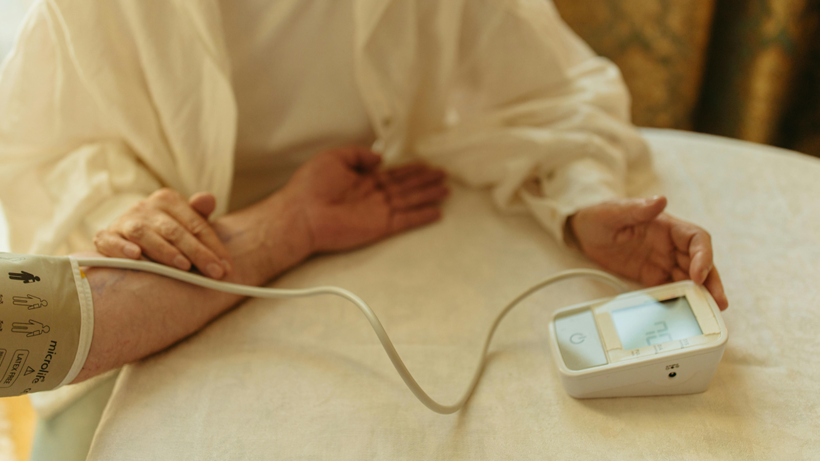 A person having their blood pressure measured with a digital monitor on a white tablecloth.