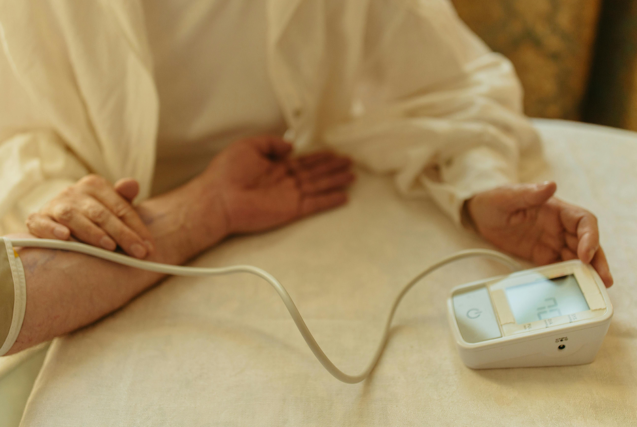 A person having their blood pressure measured with a digital monitor on a white tablecloth.