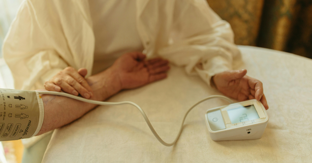 A person having their blood pressure measured with a digital monitor on a white tablecloth.