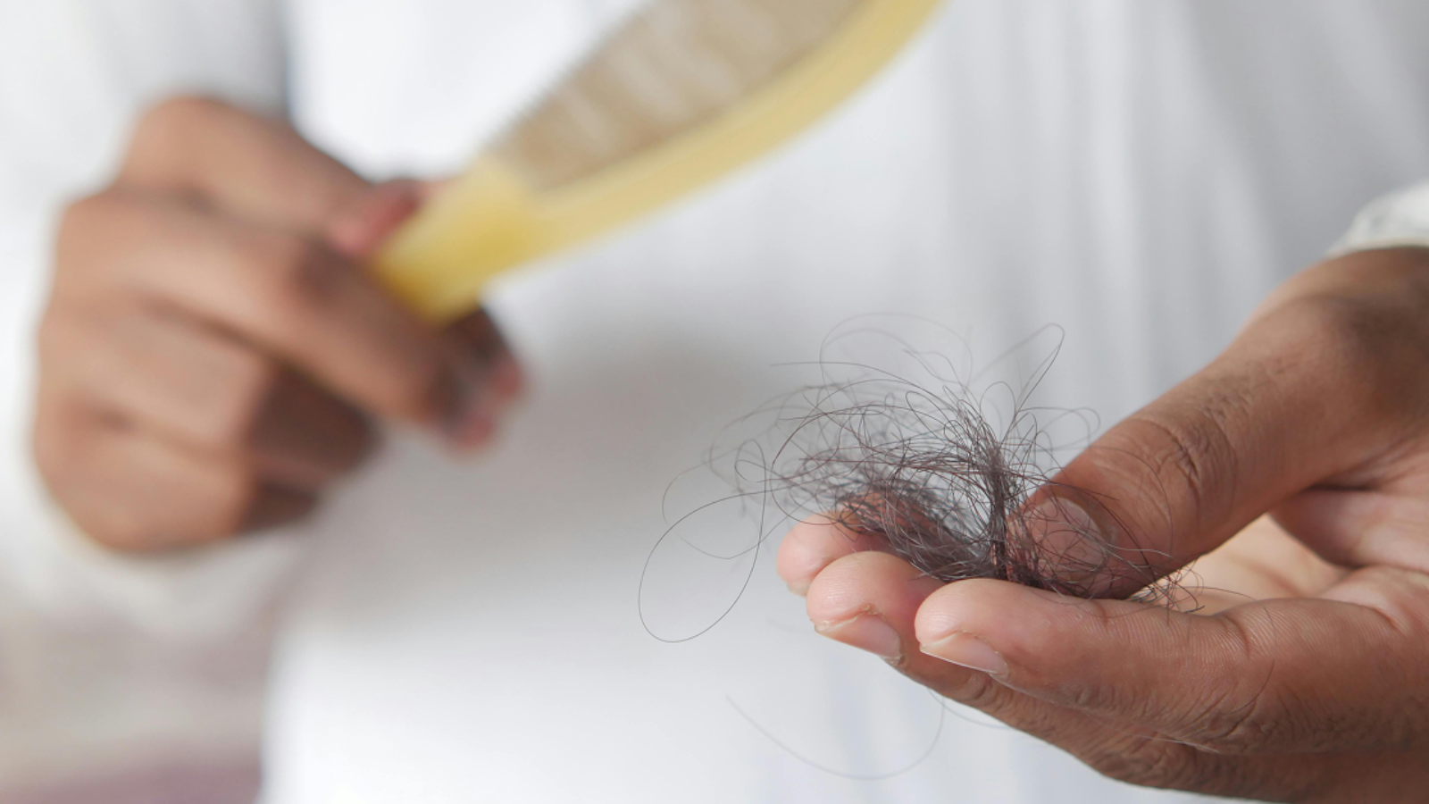 A close-up of a person holding a clump of fallen hair in their palm next to a hairbrush.