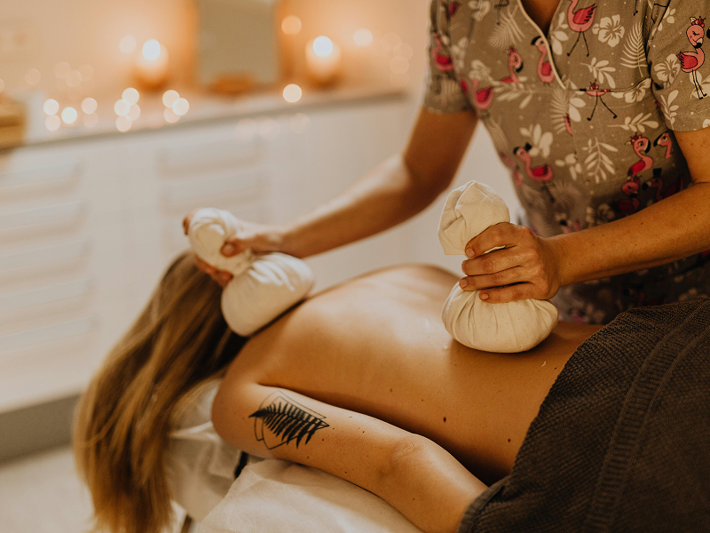 A therapist performing a Pinda Sweda massage on a client's back using two warm herbal boluses in a relaxing spa setting.